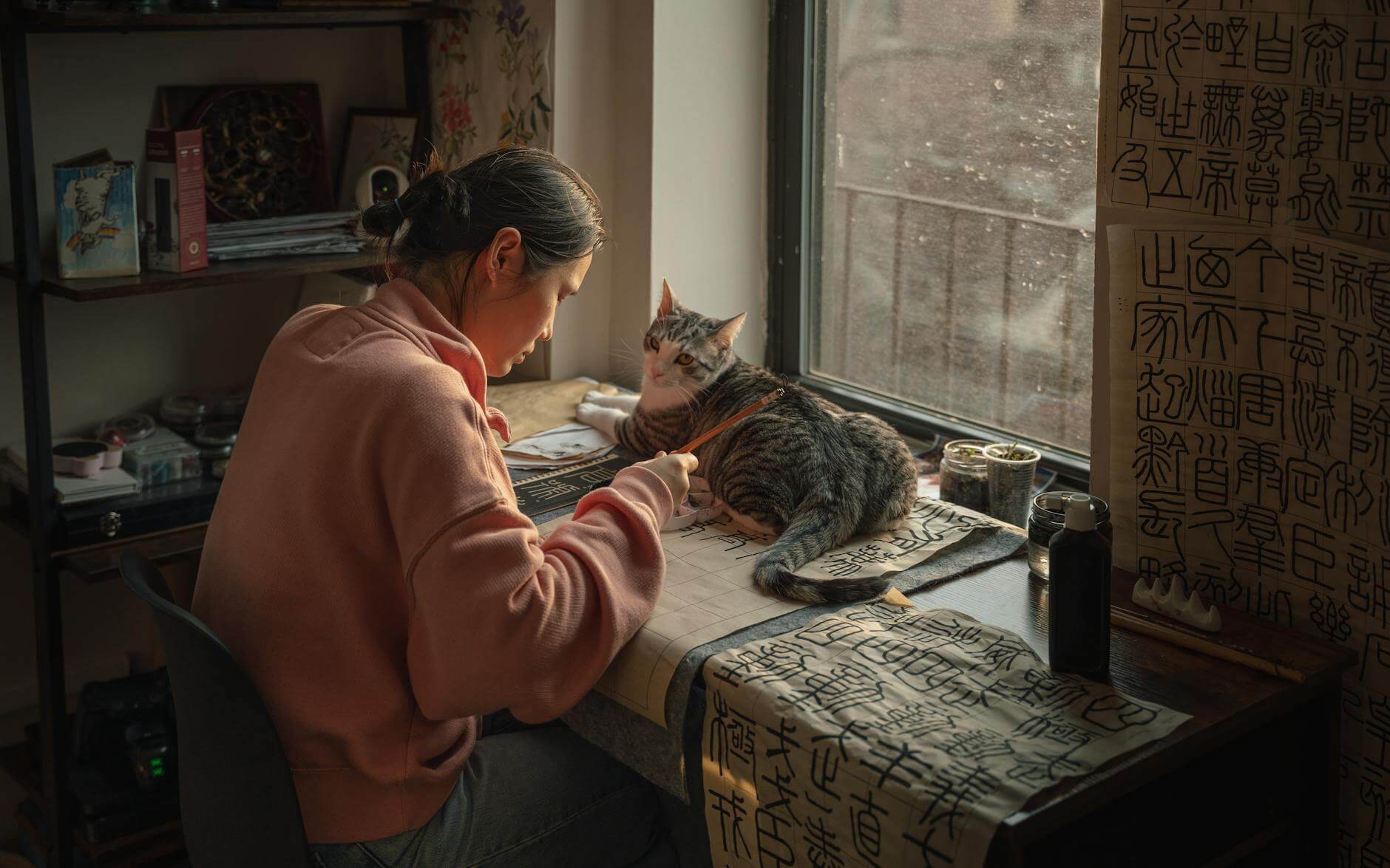 young woman practicing calligraphy with cat by window
